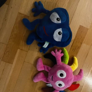 Babblarna mjukisar  - Två mjukisdjur i form av fantasifigurer. Den ena är blå med stora vita ögon och den andra är rosa med flerfärgade armar i grönt, gult och rött. Perfekta som lekfulla dekorationer eller kramgoa vänner för barn. 100kr st
