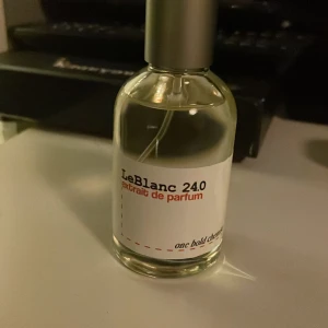 LeBlanc 240 Extrait de Parfum - Elegant och sofistikerad parfymflaska från LeBlanc med en minimalistisk design. Flaskan är genomskinlig med en silverfärgad kork och etikett i vitt med svart och röd text. Perfekt för den som söker en djärv doftupplevelse.