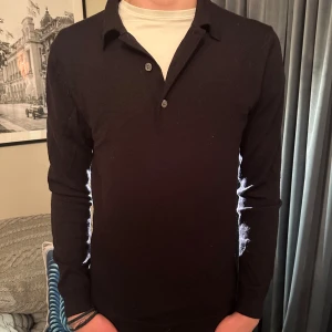 Mörkblå merinoullströja från A Day's March - Tröja med krage i merinoull från. A Day's March. Sjukt skön och passar till både en skjorta under eller T-shirt som på bilden.