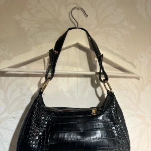 Svart axelväska  - En stilren väska som passar till nästan allt. Den får plats med mobil, plånbok, laddare etc (det man behöver)