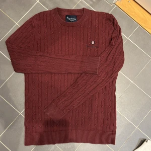 Vinröd kabelstickad tröja från Bondelid - Snygg vinröd stickad tröja med kabelmönster och rund hals. Skick 8/10. Han på bilden är 183 cm 70 kg. inga defekter