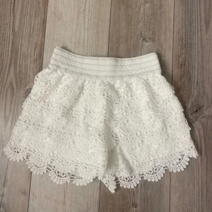 Vita spets shorts - Säljer ett par vita shorts med vacker spetsdesign och elastisk midja. Perfekta för sommarens varma dagar. De har en luftig passform och fina detaljer längs kanterna. Står storlek M/L men skulle säga att det är en S.🥰