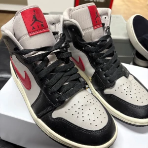 Nike Air Jordans med röd och svart design - Snygga Nike Air Jordans med en stilren kombination av svart, grå och röd. Skorna är i bra skick och är använda ungefär 10 gånger. Skorna har en klassisk snörning och den ikoniska Air Jordan-loggan på plösen. Perfekta för dig som vill ha en sportig och trendig look. 