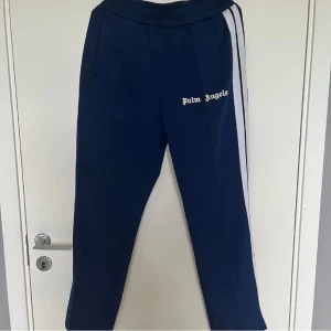 Blå byxor från Palm Angels - Snygga blå byxor från Palm Angels med vita sidoremsor och elastisk midja. Sjukt snygga och knappt använda.