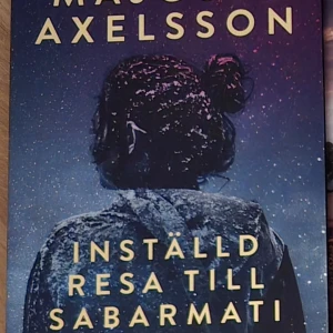 Inställd resa till Sabarmati - Boken 'Inställd resa till Sabarmati' av Majgull Axelsson har ett omslag med en bild av en person bakifrån, täckt av snö, mot en stjärnklar himmel. Titeln och författarens namn är tryckta i stora, gula bokstäver.
