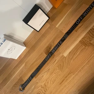 Svart bälte från Off-White - Helt ny och oanvänd Snyggt svart bälte från Off-White med märkets logga i vitt. Bältet har en modern design med en metallring som spänne. Perfekt för att ge din outfit en trendig touch.