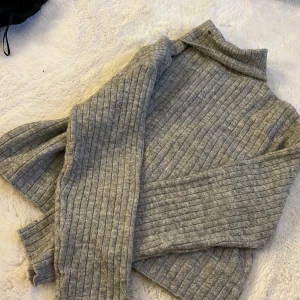 Grå ribbad polotröja från H&M - Säljer en stilren grå ribbad polotröja från H&M. Perfekt för kyliga dagar med sin mjuka och bekväma passform. Tröjan har långa ärmar och en klassisk polokrage.🩷