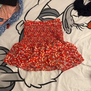 Röd blommig kjol med volang - Charmig röd kortkjol med blommigt mönster och volangdetaljer. Perfekt för en somrig look!