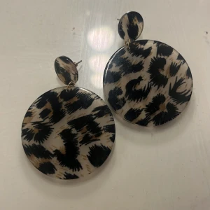 Leopardmönstrade örhängen - Snygga leopardmönstrade örhängen i rund form. Perfekta för att ge din outfit en trendig touch. De har en stilren design med en mix av svart och beige färg.