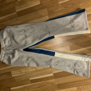 Grå mjukisbyxor med blå och vita detaljer - Snygga grå mjukisbyxor med unika stjärnmönster och kontrasterande blå och vita sidopaneler. Perfekta för en avslappnad stil med en twist.