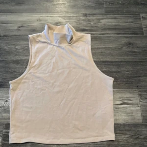 Beige ärmlös polotopp från Gina Tricot - Säljer en stilren beige ärmlös polotopp från Gina Tricot. Perfekt för lager-på-lager eller som den är under varmare dagar. Toppen har en mjuk och bekväm passform.