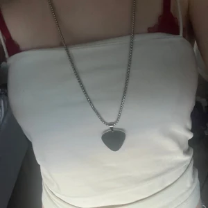 Silverfärgat halsband med plektrum berlock - Snyggt silverfärgat halsband med en plektrum berlock. Perfekt för att ge en snygg touch till din outfit. Kedjan är ganska lång och berlocken har en slät yta.