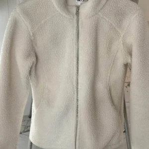 Vit fleecejacka med dragkedja - Mysig vit fleecejacka med dragkedja framtill. Perfekt för kyliga dagar med sin mjuka och varma känsla. Jackan har en enkel design med långa ärmar och en hög krage. Det är en tröja från Aim’n som är super fin och perfekt inför vintern eller skiftet mot våren.  Använd väldigt få gånger men är i bra skick. 