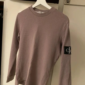 Beige tröja från Calvin Klein Jeans - Säljer en stilren beige tröja från Calvin Klein Jeans med långärmad design. Tröjan har en CK-logga på ärmen och är tillverkad i ett mjukt material som ger en bekväm passform. Perfekt för en avslappnad look.