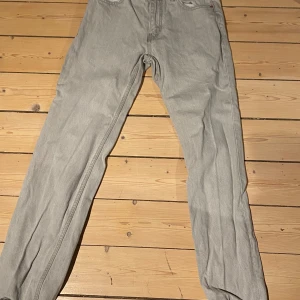 Grå jeans från Gina tricot  - Snygga grå jeans från Gina tricot storlek M. De har en klassisk design med knapp och dragkedja framtill. Perfekta för en stilren look.