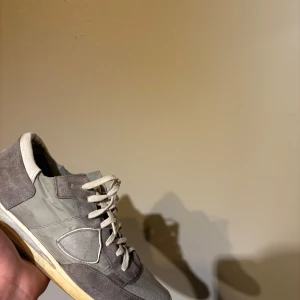 Grå sneakers från Philippe Model - Snygga grå sneakers från Philippe Model med en stilren design. Skorna har snörning och är tillverkade i en kombination av mocka och syntetmaterial. Perfekta för en avslappnad stil.