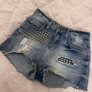 Blå jeansshorts med nitar - Snygga blå jeansshorts med slitna detaljer och nitar på framsidan. Från Gina tricot i st XS