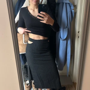 Svart midikjol med vita ränder - Snygg svart midikjol med vita ränder och unika utskärningar i midjan. 