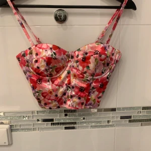 Blommig korsettopp från Amisu - Snygg blommig korsettopp från Amisu i rosa, rött och lila med justerbara axelband och dragkedja bak. Perfekt för en somrig look!