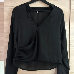 Svart blus från Nelly - En svart blus från Nelly. Superfin men inte kommit till användning på senaste. Finns tecken på användning vid omlottdelen då någon tråd på kanten/insidan börjat lossna, kolla bild 3. Men  inget som syns direkt. 
