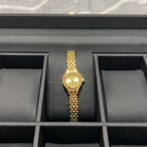 Guldfärgad damklocka - Snygg guldfärgad klocka med en klassisk design. Den har en länkarmband och en rund urtavla som ger en tidlös look. Perfekt för att lägga till en touch av elegans till din stil.