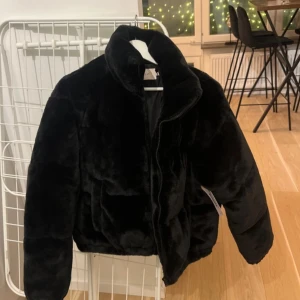 Padded fur jacket Nelly - Snygg och trendig svart pälsjacka från Nelly.Jackan är fodrad har en hög krage för extra värme. Perfekt för kyliga dagar när du vill se både stilren och mysig ut.🎀SLUTSÅLD PÅ HEMSIDAN. HELT OANVÄND MED PRISLAPP.