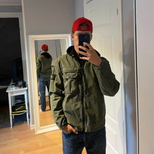 Grön jacka från Stone Island - Säljer en snygg olivgrön jacka från Stone Island. Den har en dragkedja framtill och en praktisk bröstficka med knapp. Perfekt för höst och vår, med en stilren design och Stone Islands ikoniska märke på ärmen. Jackan är i storlek S och har även taggen inuti. Den är lite sliten i färgen solblekt/urtvättad.