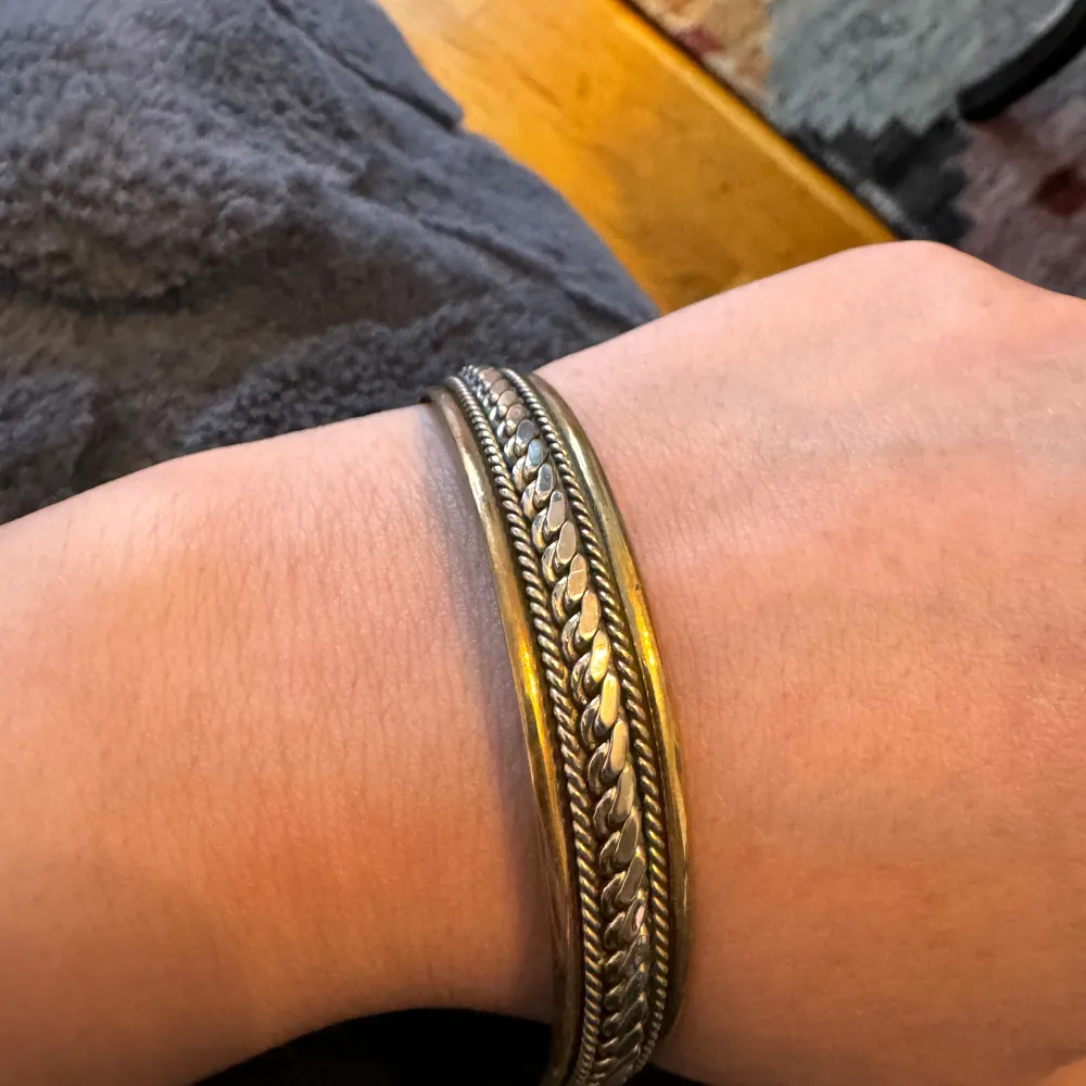 Säljer ett snyggt vintage armband i silver och guld. Armbandet har en flätad design och är öppet i ändarna vilket gör det justerbart. Perfekt för att ge en elegant touch till din outfit!. Accessoarer.