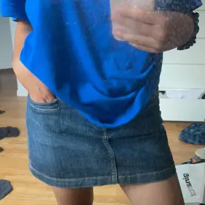 Säljer en snygg och klassisk jeanskjol i blå denim. Kjolen är kort och har en normal passform med knäppning fram. Den har två fickor både fram och bak. 