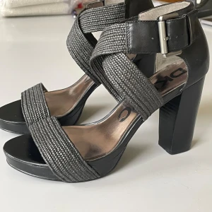 DKNY högklackade svarta skor - DKNY svarta skor med 10 cm hög klack. Stängs med en rem runt ankeln. Endast använda ett fåtal gånger så de är i nyskick.