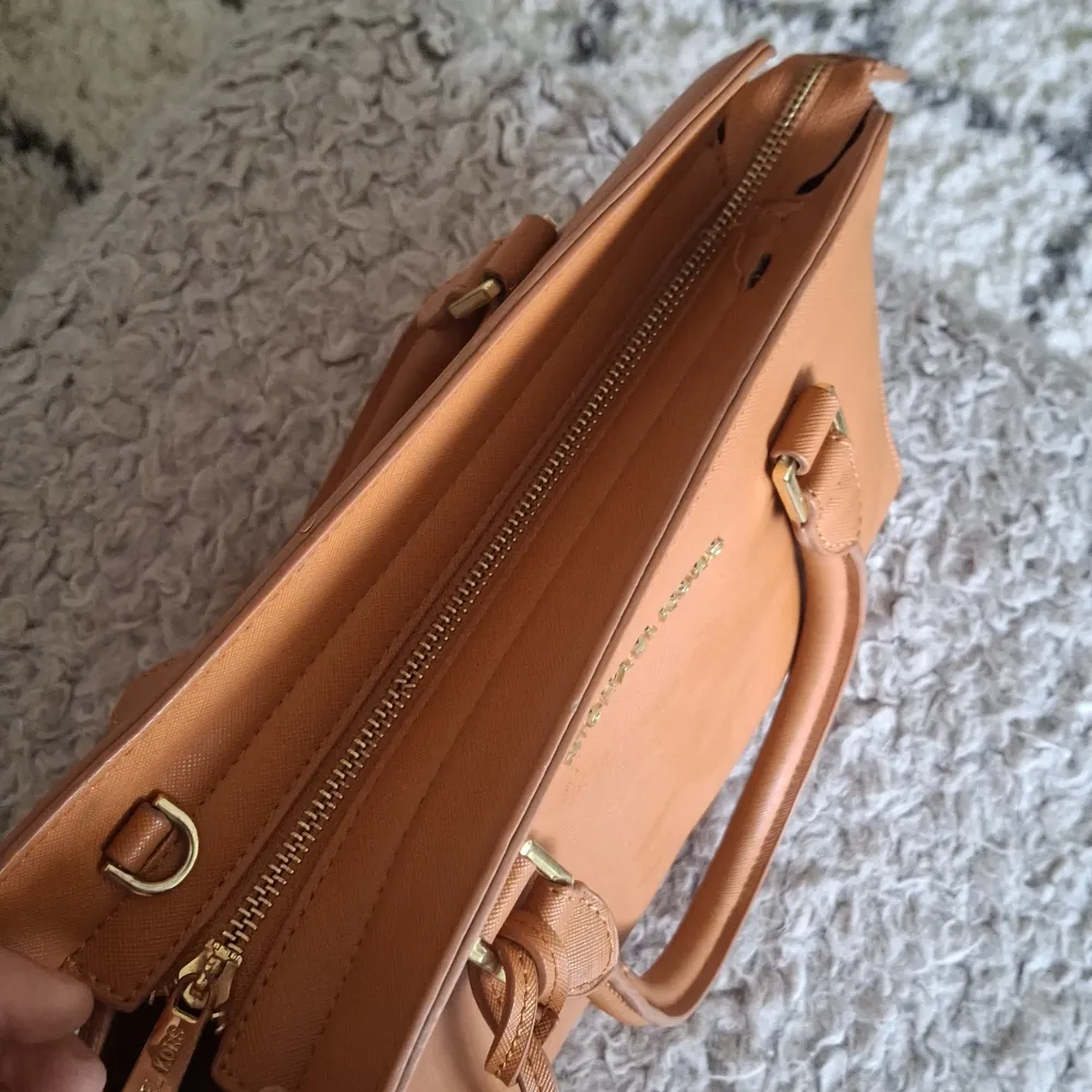 Säljer en snygg brun handväska från Michael Kors. Väskan har en elegant design med guldiga detaljer. Den har två handtag och en dragkedja upptill för säker förvaring. Perfekt för både vardag och fest! 👜✨obs axelbandet saknas, liten defekt enligt bild . Laukut & Käsilaukut.