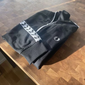Fred Perry Taped Track Jacka Svart - Fred Perry jacka i toppskick, har använts ett fåtal gånger och har inga skador eller fläckar. Säljer då jag inte längre använder den. Original pris 1499kr