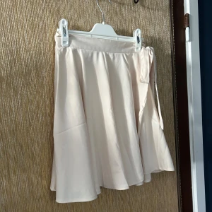 Beige omlottkjol - Säljer en superfin beige omlottkjol. Den är i ett mjukt och lätt material, perfekt för varma dagar. Kjolen har en knytning på sidan som ger en söt detalj och gör att den sitter bra på plats. Den är i nyskick och passar perfekt till både vardag och fest.😊