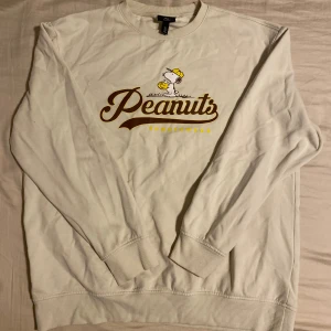 Beige/vit Peanuts tröja från H&M - Långärmad beige sweatshirt från H&M med tryck både fram och bak. Tveka inte att höra av dig om du har frågor eller vill ha fler bilder!
