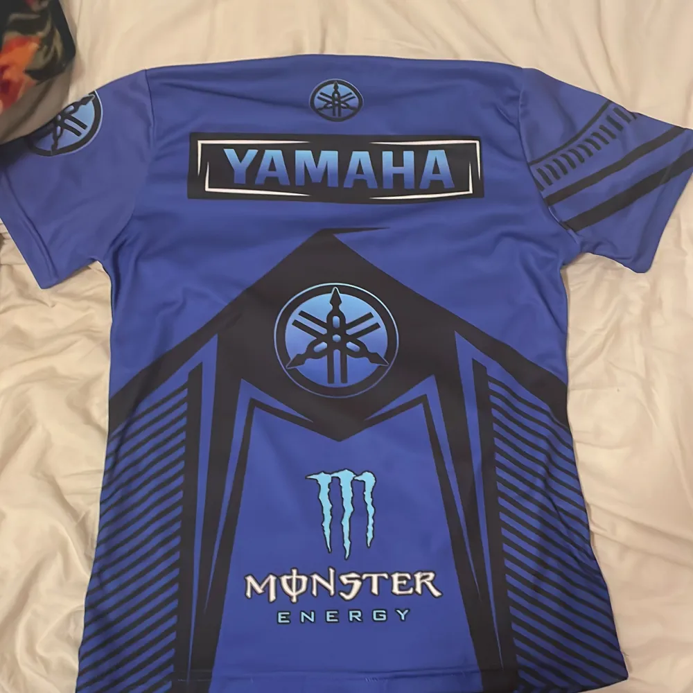 Säljer en blå Yamaha t-shirt med coola tryck och Monster Energy-logga. T-shirten har korta ärmar och är perfekt för motorcykelentusiaster. Den har en sportig design med svarta och blå detaljer samt texten 'Revs Your Heart'.. T-paidat.