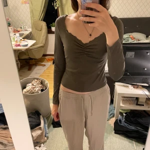 Grå långärmad topp med v-ringning - Säljer en snygg grå långärmad topp med v-ringning och rynkdetalj framtill. Toppen är figurnära och perfekt för både vardag och fest. Materialet är mjukt och stretchigt, vilket gör den superbekväm att ha på sig. Passar perfekt till ett par jeans eller kjol!