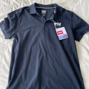 Mörkblå pikétröja från Helly Hansen - Säljer en snygg mörkblå pikétröja från Helly Hansen. Den är i nyskick med lappen kvar. Perfekt för både vardag och lite mer uppklädda tillfällen. Tröjan är gjord i ett bekvämt material som känns skönt mot huden. Frågor? Skriv!