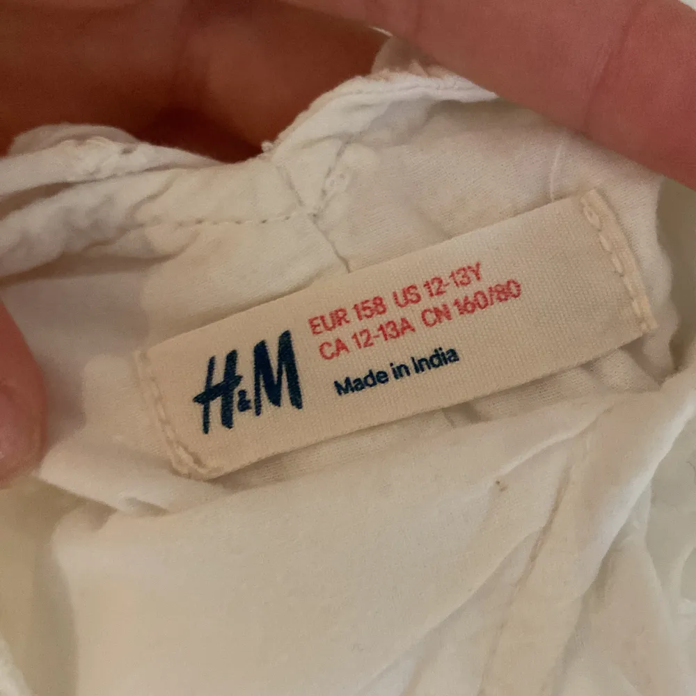 Säljer en söt vit sommarklänning från H&M. Klänningen är ärmlös och har en smockdetalj i midjan som ger en fin passform. Den är tillverkad i ett lätt och luftigt material, perfekt för varma sommardagar. Klänningen har en v-ringad hals och en liten volangdetalj vid axlarna. Perfekt för både vardag och fest!. Klänningar.