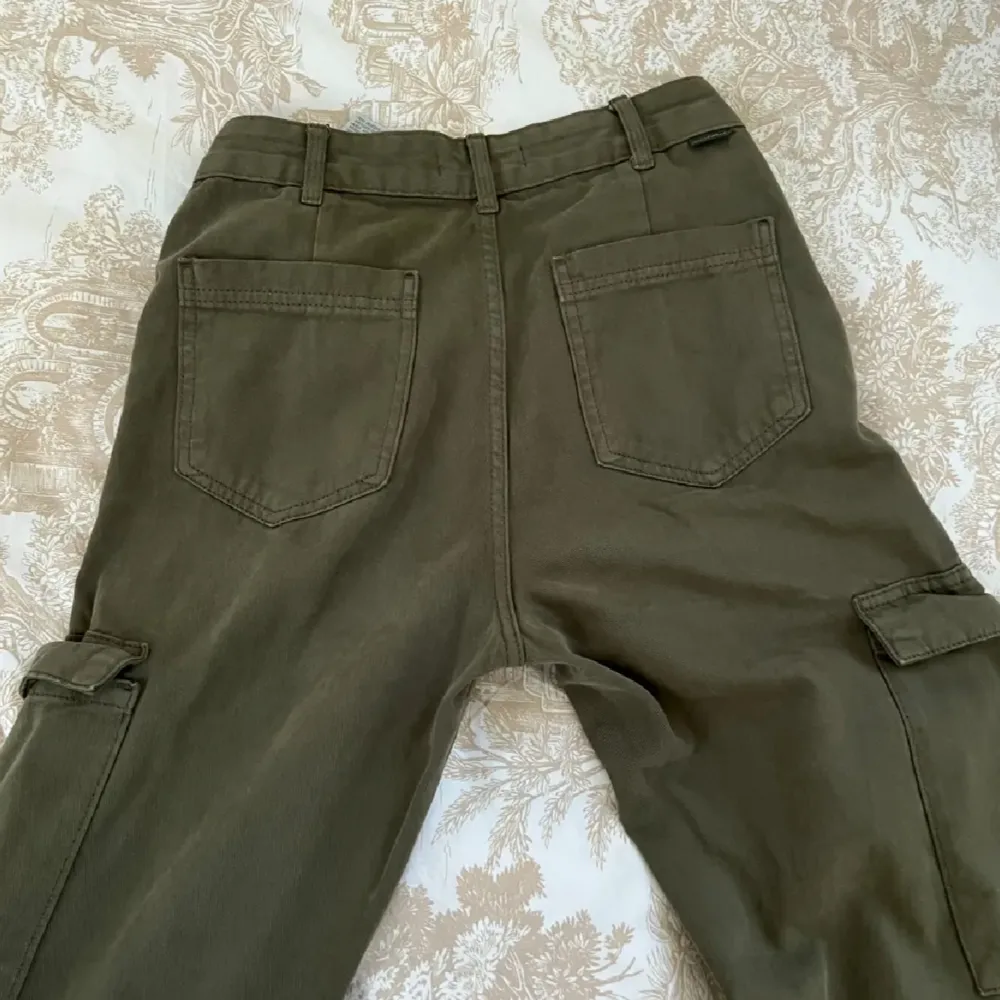 Säljer ett par olivgröna cargopants från PULL&BEAR. Byxorna har flera praktiska fickor, inklusive två stora sidofickor med lock. De är tillverkade i ett slitstarkt bomullsmaterial och har en normal passform. Perfekta för en casual look eller utomhusaktiviteter. Köp direkt eller ge prisförslag 💚. Jeans & Byxor.