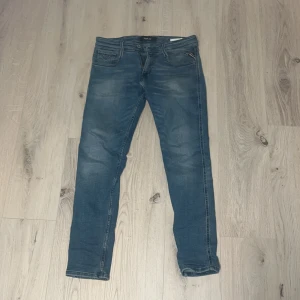 Blå replay anbass jeans - Snygga blå jeansbyxor med en klassisk design. De har en normal passform och är perfekta för en avslappnad stil. Byxorna har en dragkedja och knapp framtill. En liten defekt som man ser i bild 3. 