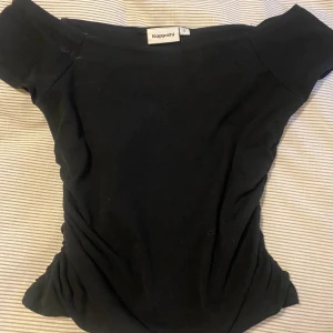 Svart offshoulder topp från Kappahl - Snygg svart offshoulder topp från Kappahl. Perfekt för en stilren look med korta ärmar och en bekväm passform. Enkelt att matcha med olika outfits.