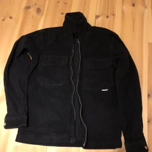 Svart manchesterjacka från Yôke - Snygg svart manchesterjacka från Yôke med dragkedja och två stora bröstfickor. Jackan har långa ärmar och en stilren design som passar perfekt för höst och vår. Perfekt för dig som vill ha en stilren look. Storlek S utan några skador.