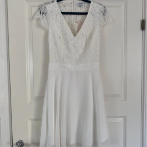 Vit studentklänning från Bubbleroom - Studentklänning från Bubbleroom med v-ringning och spetsdetaljer. Klänningen har korta ärmar och en öppen rygg med knappar. Klänningen är i storlek 34 och är helt oanvänd, dragkedja finns även på sidan.🩷pris går att diskutera!