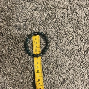 Grönt armband med pärlor - Snyggt grönt armband med runda pärlor och en mörkare detalj. Perfekt för att ge en naturlig touch till din stil. Passar bra till både vardag och speciella tillfällen.Helt ny så kostade den 130kr