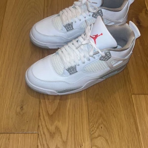 Vita Nike Air Jordans - Snygga vita Nike Air Jordans med grå detaljer och snörning. Skorna har en ikonisk design med synlig luftdämpning i sulan och det klassiska Jumpman-logotypen på hälen. Perfekta för dig som vill ha en stilren look. (Ingen box tyvärr)