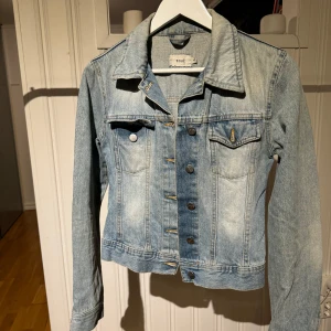 Jeansjacka från Zoul - Snygg jeansjacka från Zoul i en klassisk blå tvätt. Jackan har knappar framtill och två bröstfickor med lock. Perfekt för vår och sommar, med en stilren och tidlös design.