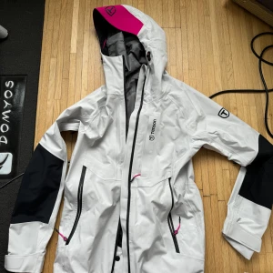 Vit skidjacka från Tenson XS-S - Säljer en vit vindjacka från Tenson med svarta detaljer och rosa på huvan. Jackan har dragkedja och flera praktiska fickor. Perfekt för skidåkning! Säljer på grund av fel storlek. Ord pris 2,7k. Kan gå ned i pris vid snabb affär 