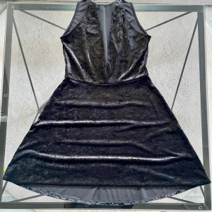 Svart sammet klänning - Snygg svart klänning i sammet med djup v-ringning. Perfekt för en elegant look. Klänningen har en kort längd och är ärmlös, vilket ger en stilren och modern känsla.