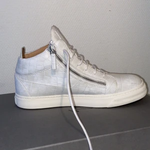 Vita sneakers med krokodilmönster och dragkedja - Snygga vita Giuseppe Zanottis med krokodilmönster och dragkedja på sidan. Skorna har snörning och en stilren design som passar perfekt för en trendig look.