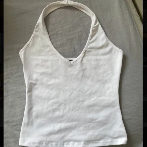 Vit ärmlös halterneck-topp - Säljer en supersöt vit halterneck-topp med v-ringning. Kommer inte till användning. Den har inga defekter.